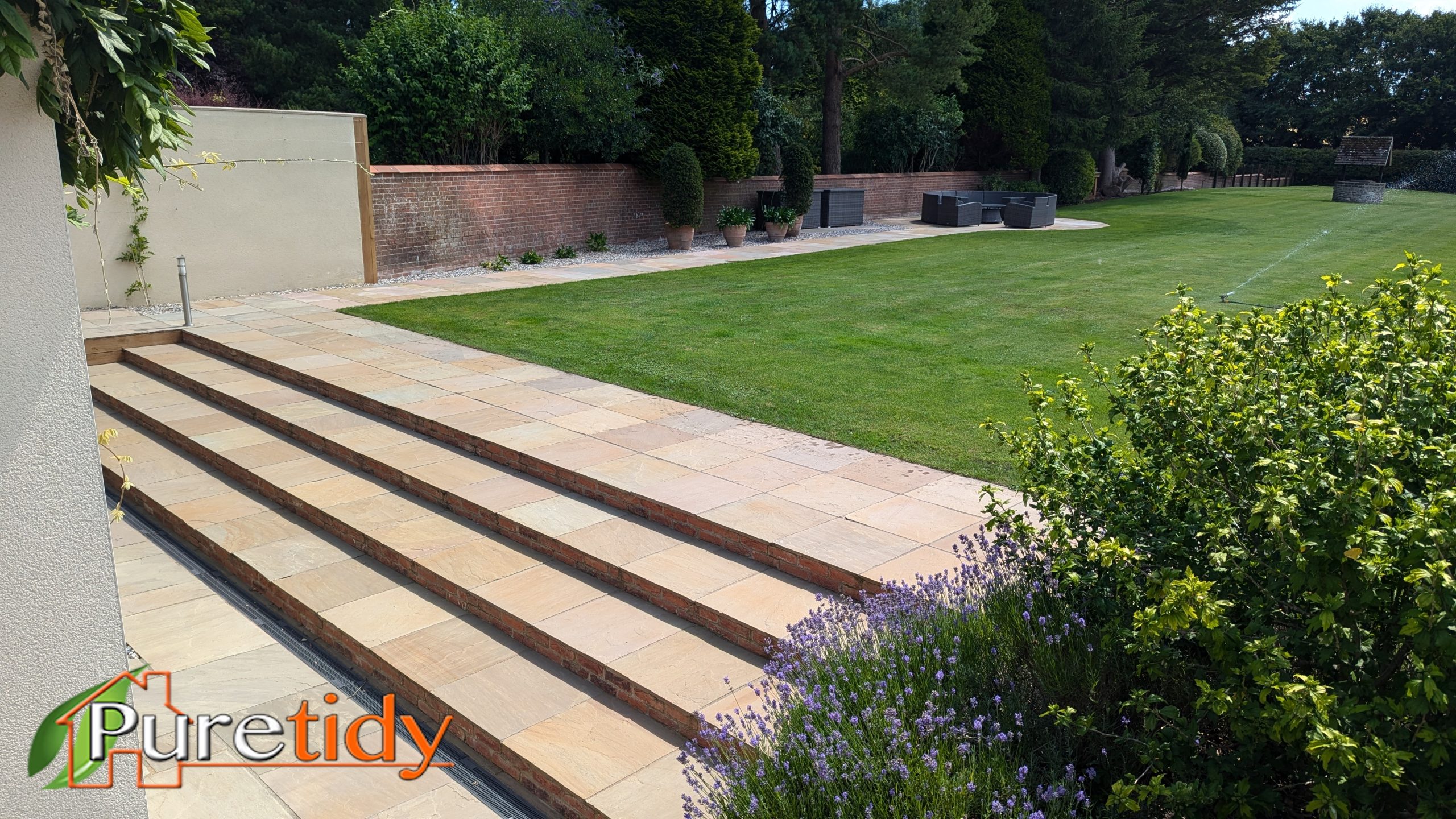Newly installed sandstone patio steps leading up to a lush green lawn in a Wanborough garden by Puretidy